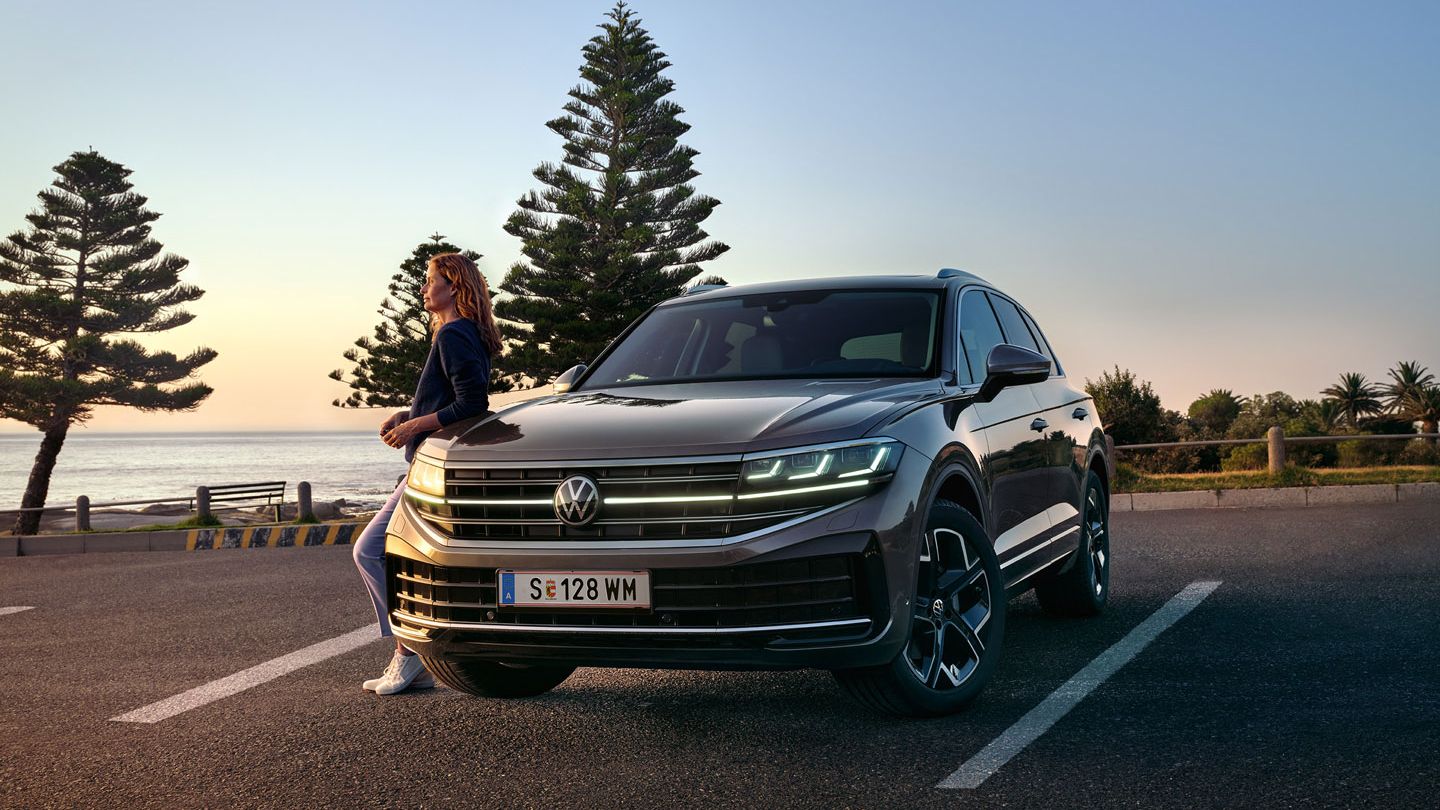 Ein VW Touareg Elegance in der Dämmerung am Meer mit eingeschalteten HD-Matrix-Scheinwerfern. 