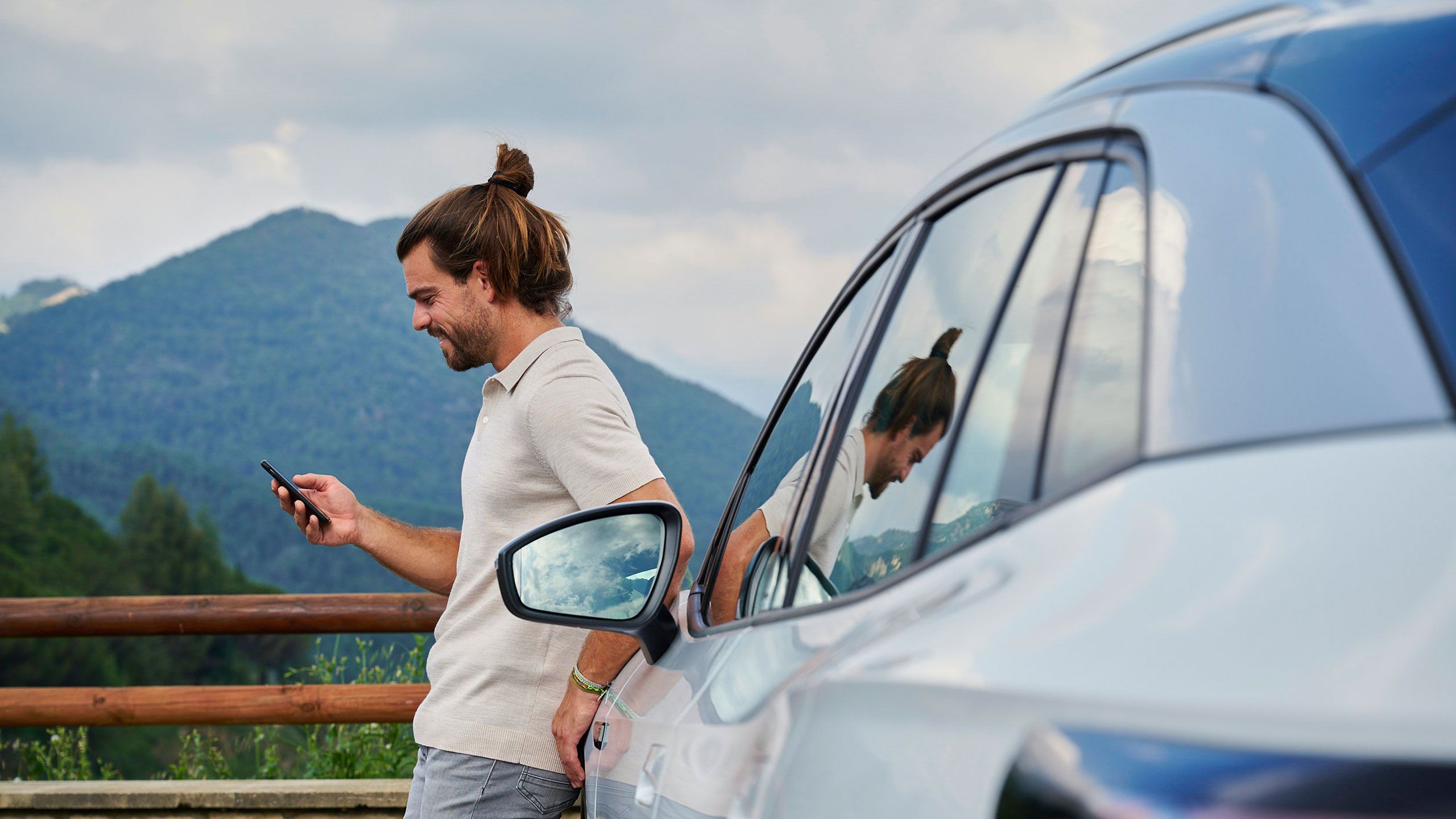 Ein Mann lehnt an einem Volkswagen ID. und blickt auf sein Smartphone.