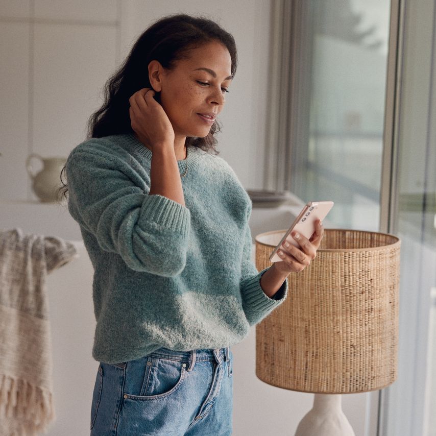 Eine Frau steht am Fenster und blickt auf ihr Smartphone