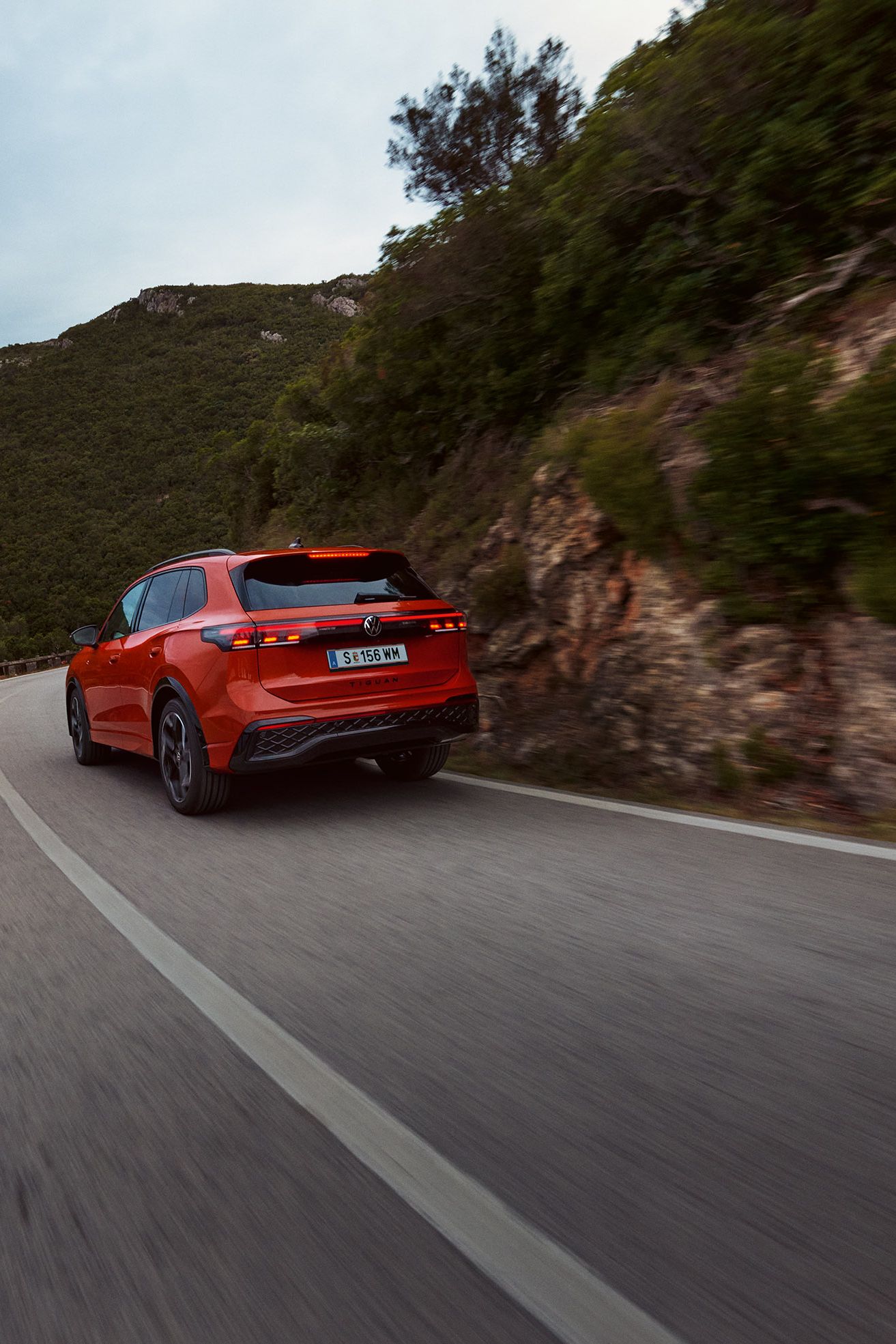 Roter VW Tiguan in Heckansicht fährt durch eine bergige Landschaft.