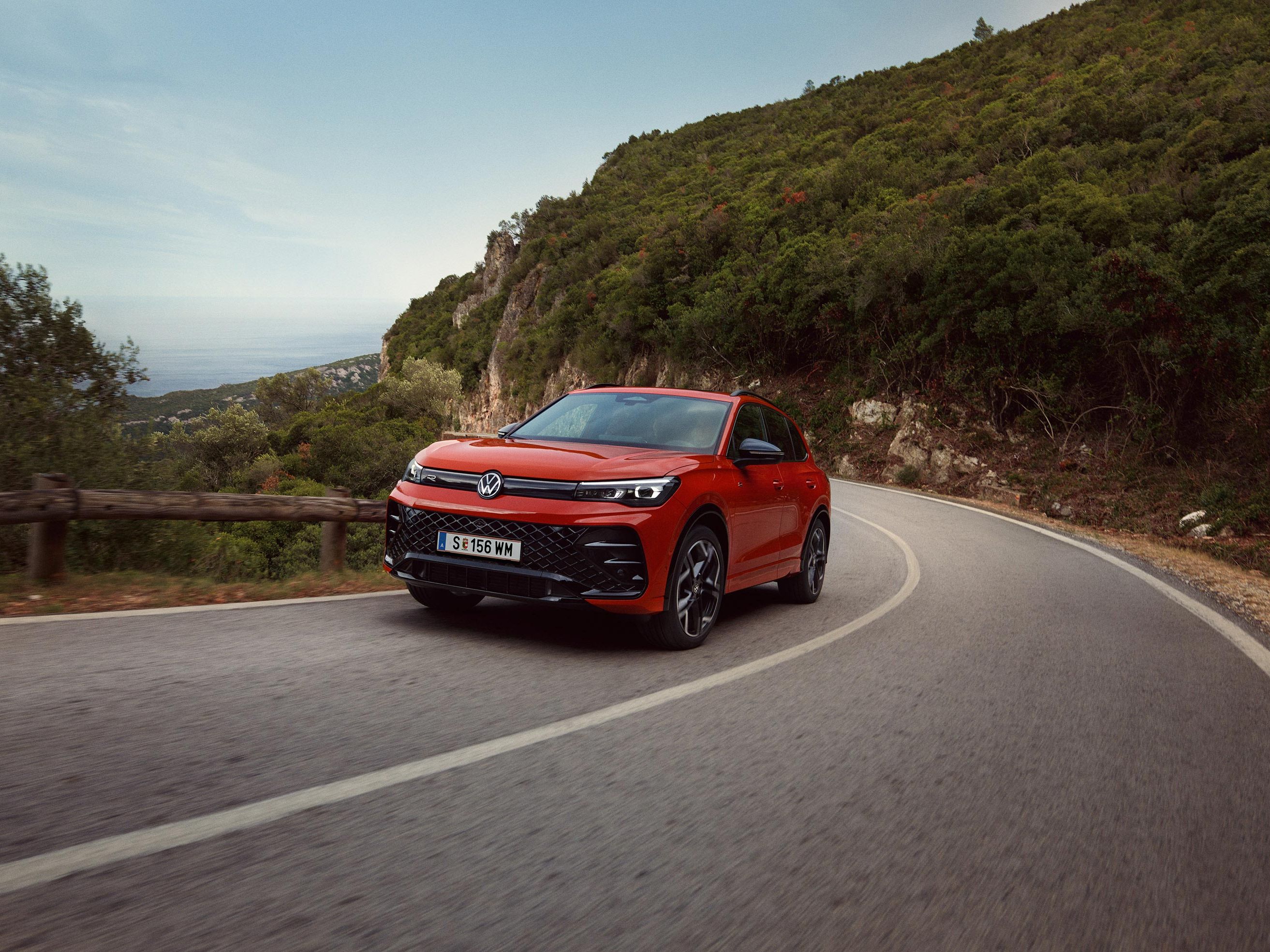 Roter VW Tiguan R-Line fährt eine kurvige Straße entlang.