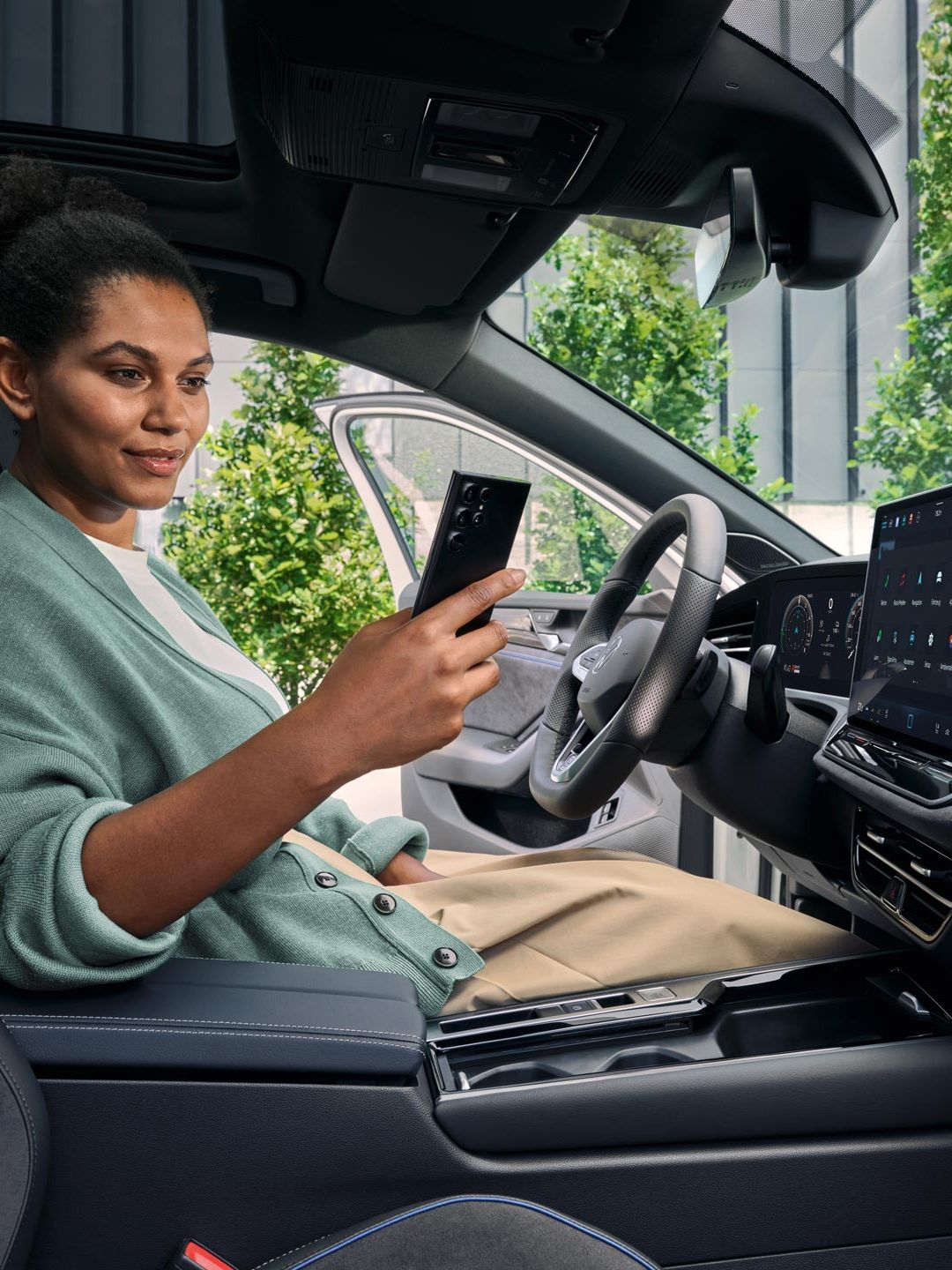 Eine Frau sitzt bei geöffneter Tür auf dem Fahrersitz des geparkten VW Passat und blickt auf ihr Smartphone.