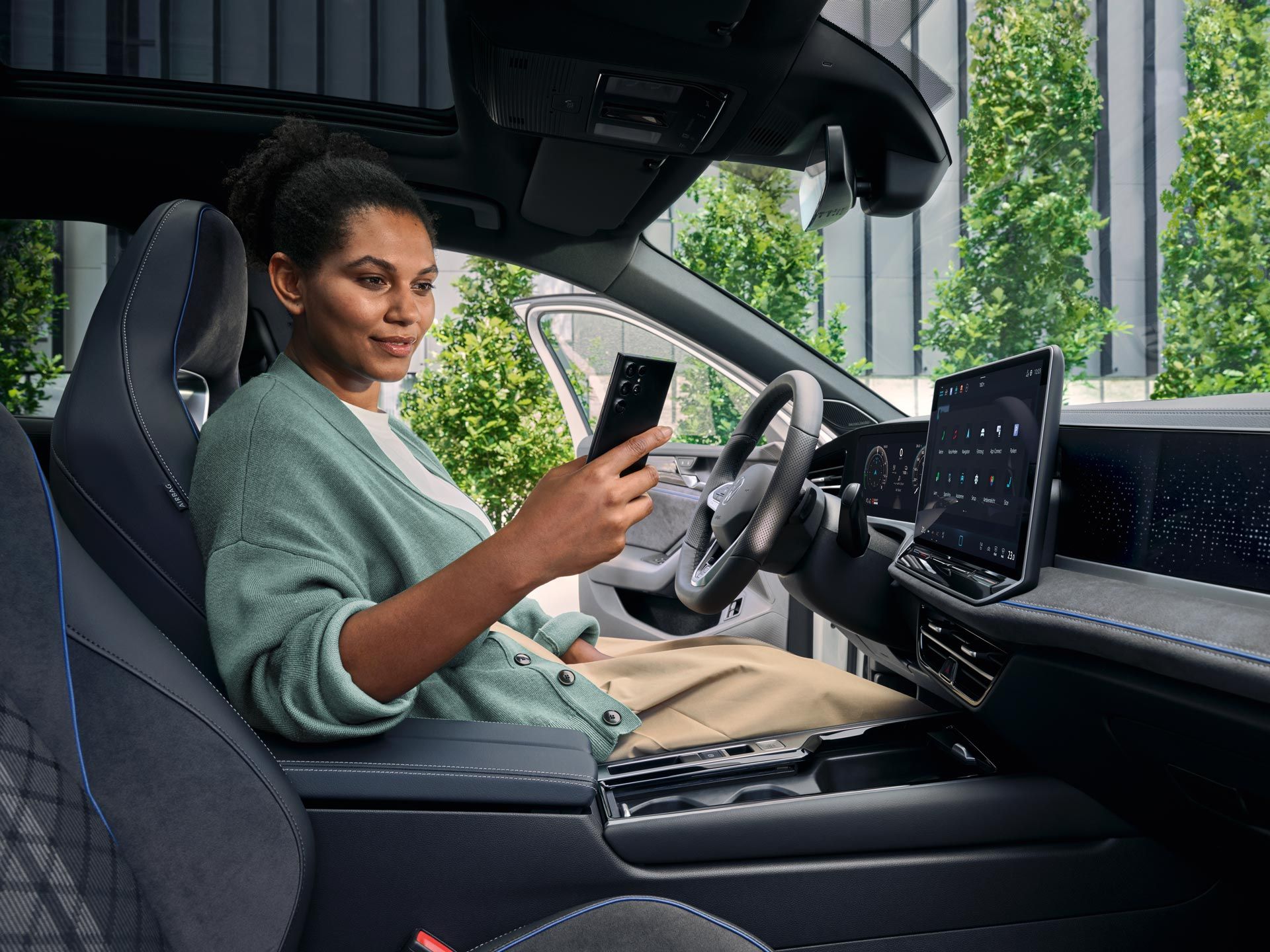 Eine Frau sitzt bei geöffneter Tür auf dem Fahrersitz des geparkten VW Passat und blickt auf ihr Smartphone.