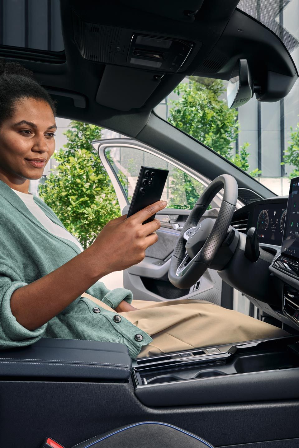 Eine Frau sitzt bei geöffneter Tür auf dem Fahrersitz des geparkten VW Passat und blickt auf ihr Smartphone.