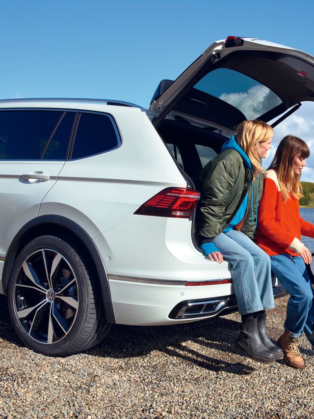 Zwei Frauen sitzen auf der Kofferraumkante des VW Tiguan Allspace und unterhalten sich mit einem Mann