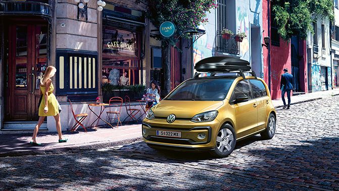 Ein gelber VW up! mit Dachbox fährt auf einer Straße