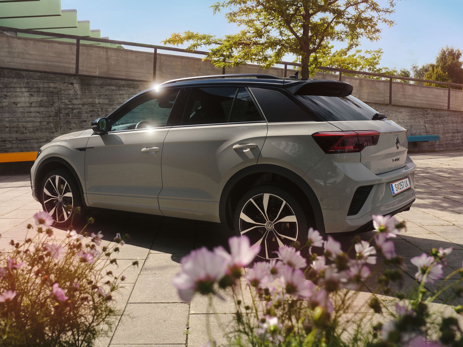 Blick auf die linke Seite und das Heck vom VW T-Roc, im Vordergrund blühen rosa Blumen 