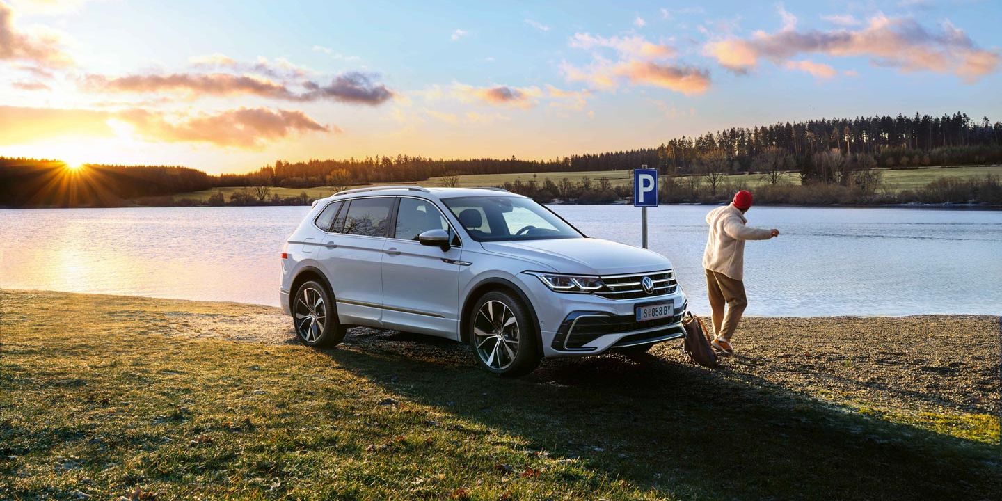 Mann steht neben einem weißen VW Tiguan Allspace, der am Seeufer geparkt ist