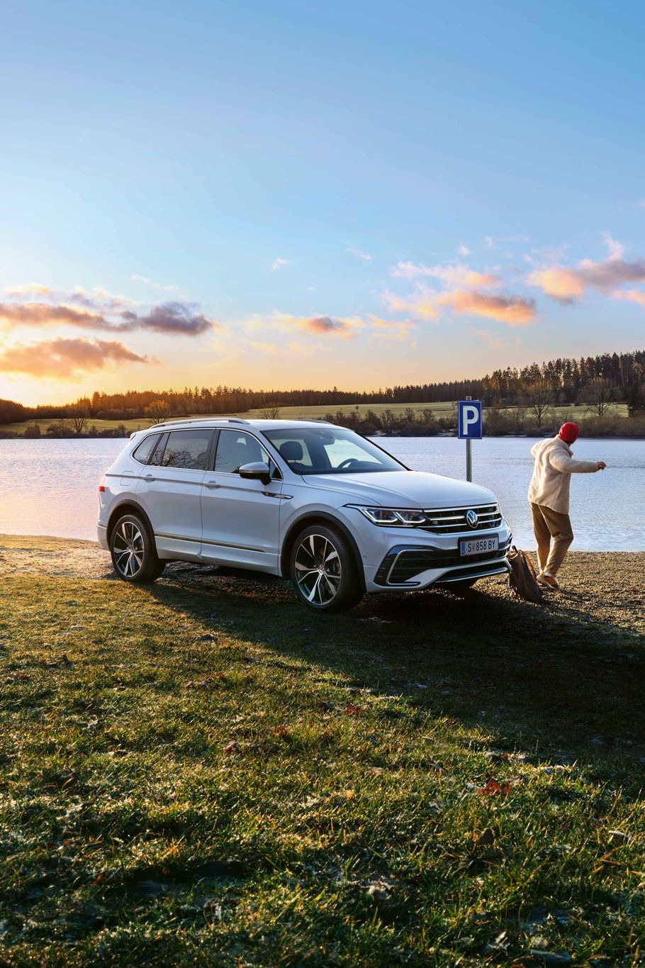 Mann steht neben einem weißen VW Tiguan Allspace, der am Seeufer geparkt ist