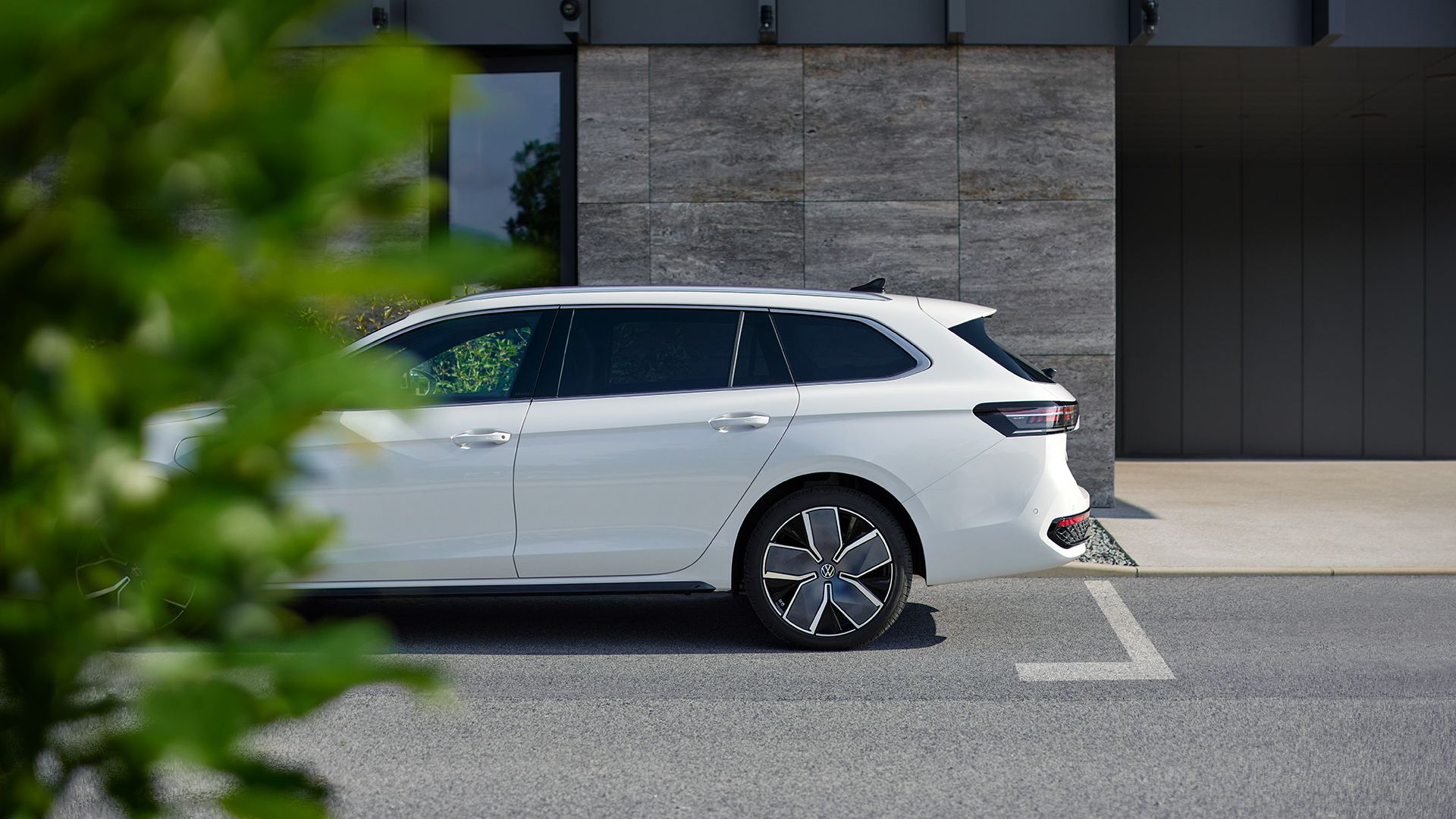 Ein weißer VW Passat steht geparkt vor einem Haus, die Front ist leicht durch einen Busch im Vordergrund verdeckt