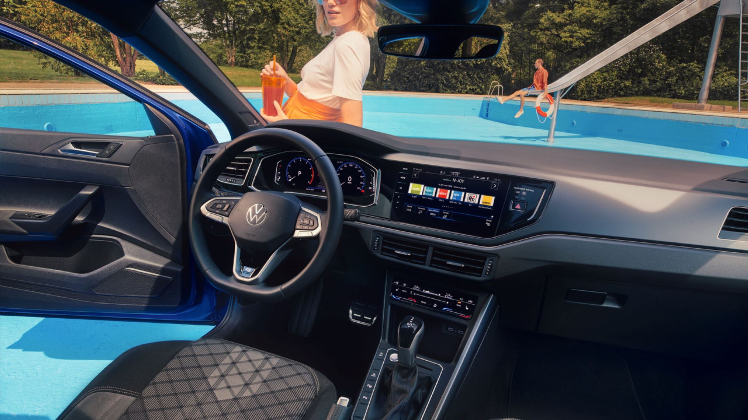 Interieur des VW Polo mit Infotainmentsystem, Multifunktionslenkrad und Digital Cockpit. Blick durch die Wundschutzscheibe auf eine Frau. 