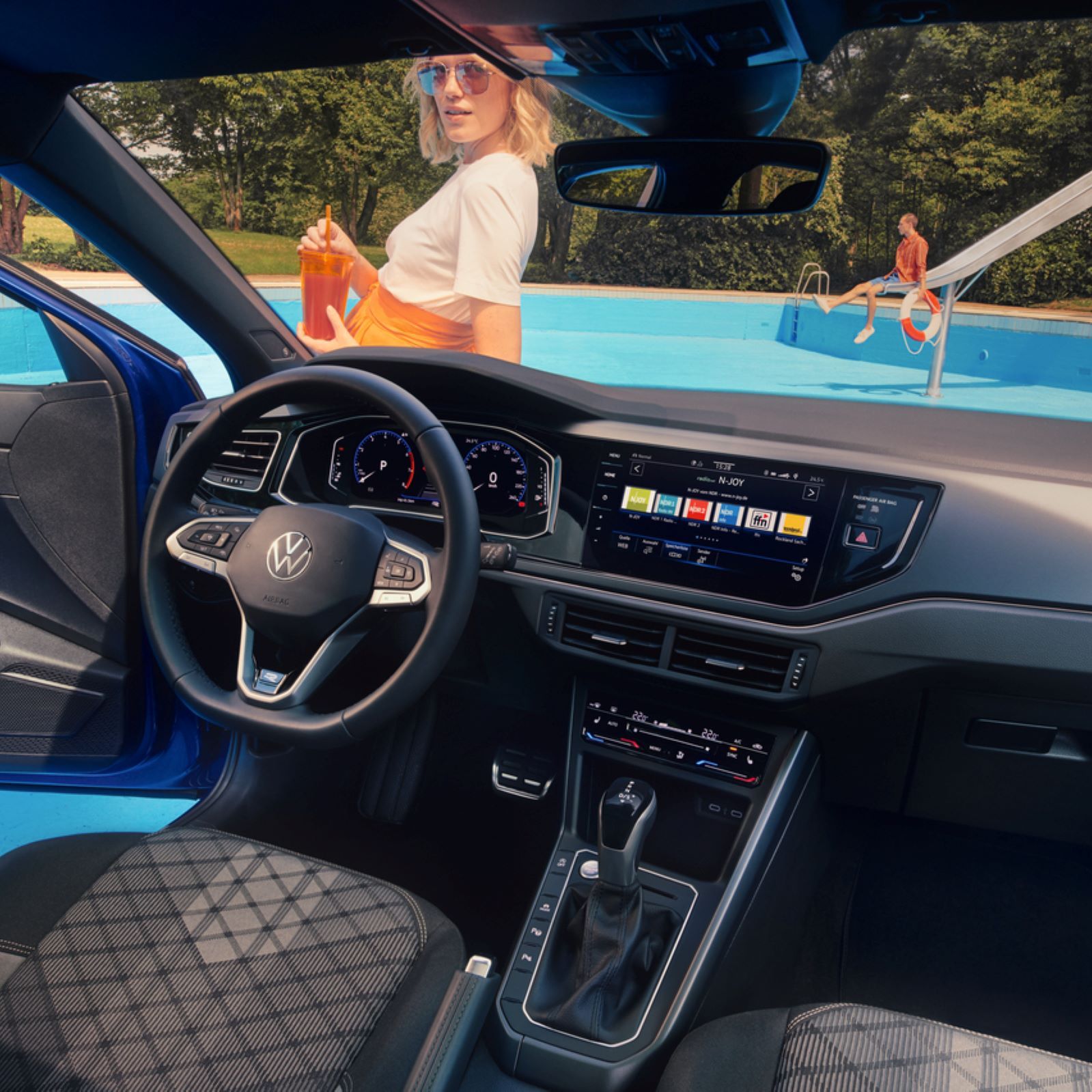 Interieur des VW Polo mit Infotainmentsystem, Multifunktionslenkrad und Digital Cockpit. Blick durch die Wundschutzscheibe auf eine Frau. 