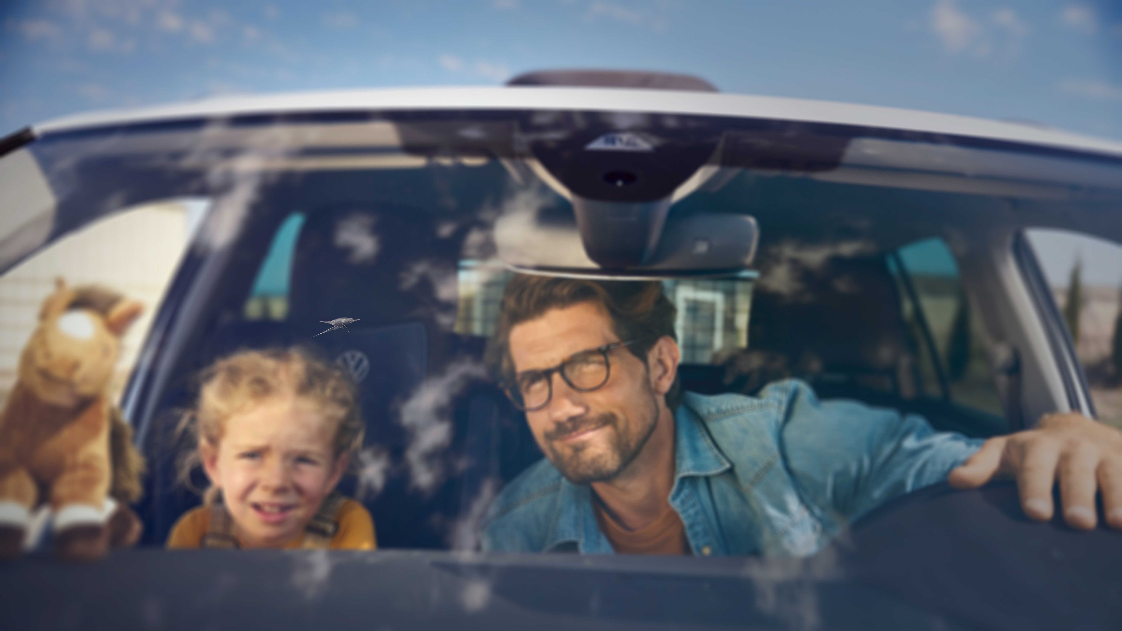 Ein Vater und seine Tochter betrachten einen Steinschlag auf der Windschutzscheibe eines Volkswagen.