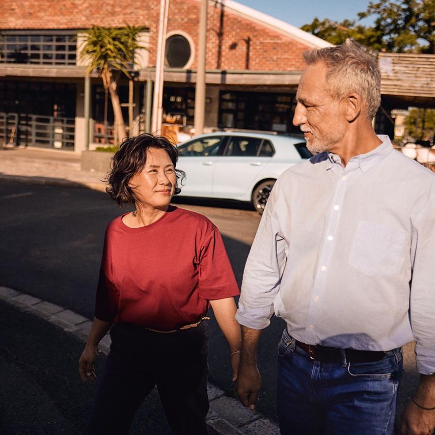 Ein Mann und eine Frau laufen gemeinsam über eine Straße, im Hintergrund parkt ein VW Golf