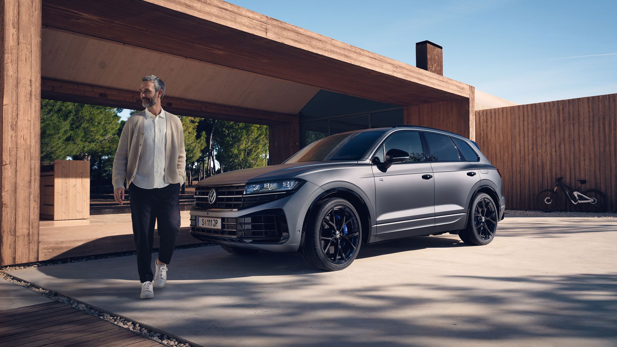 Ein VW Touareg R eHybrid parkt vor einem Haus, ein Mann bewegt sich vom Fahrzeug fort