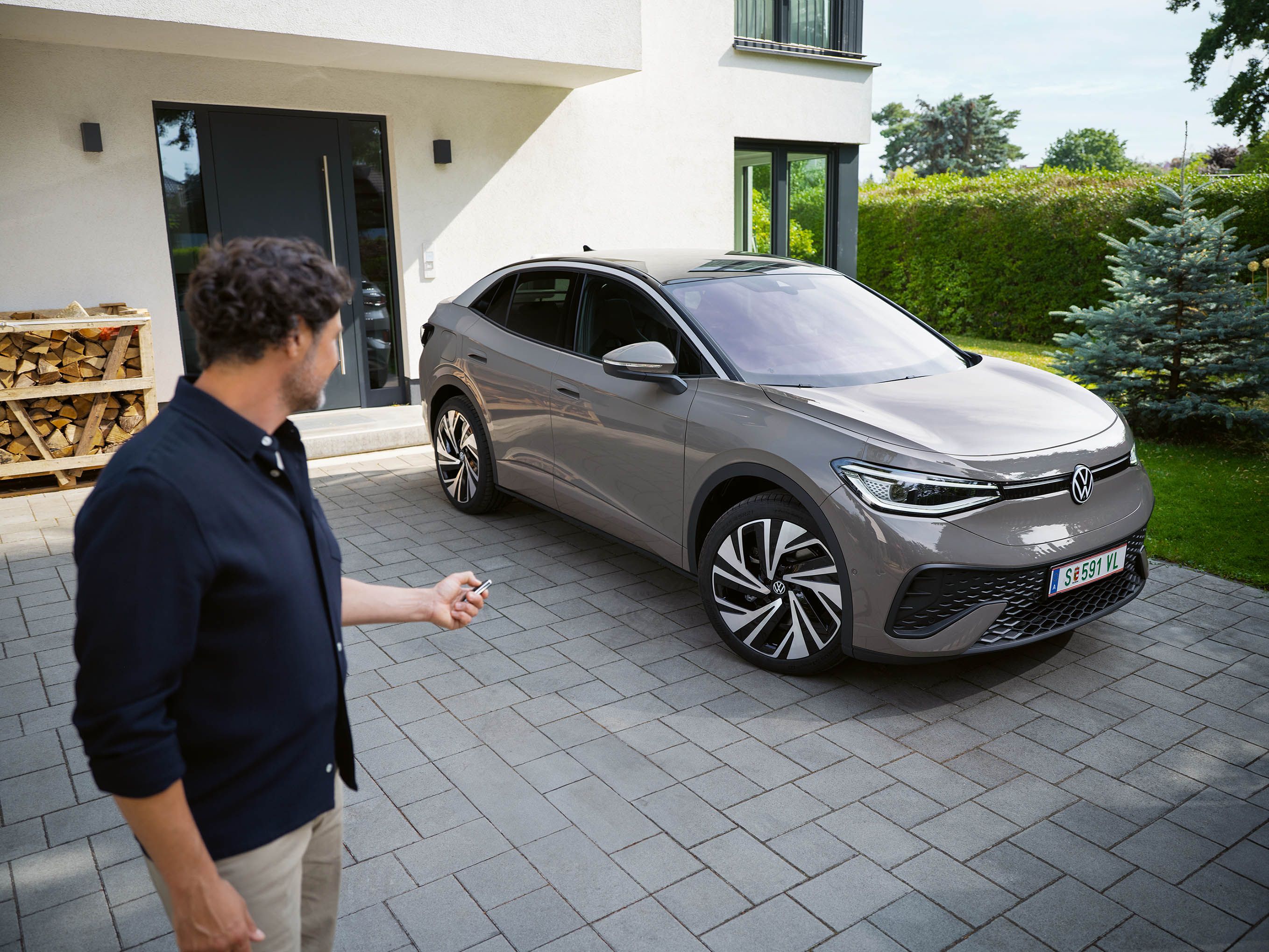 Ein grauer ID.5 steht in einer Einfahrt vor einem Haus, ein Mann schließt das Auto ab. 