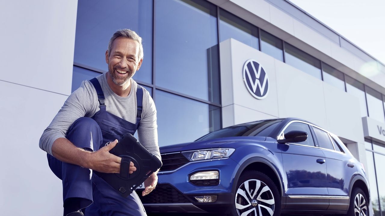 Ein Volkswagen Service Techniker mit Tablet, kniet vor einem blauen Volkswagen T-Roc