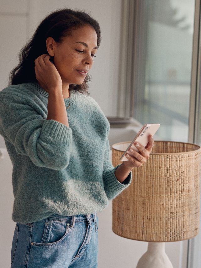 Eine Frau steht am Fenster und blickt auf ihr Smartphone