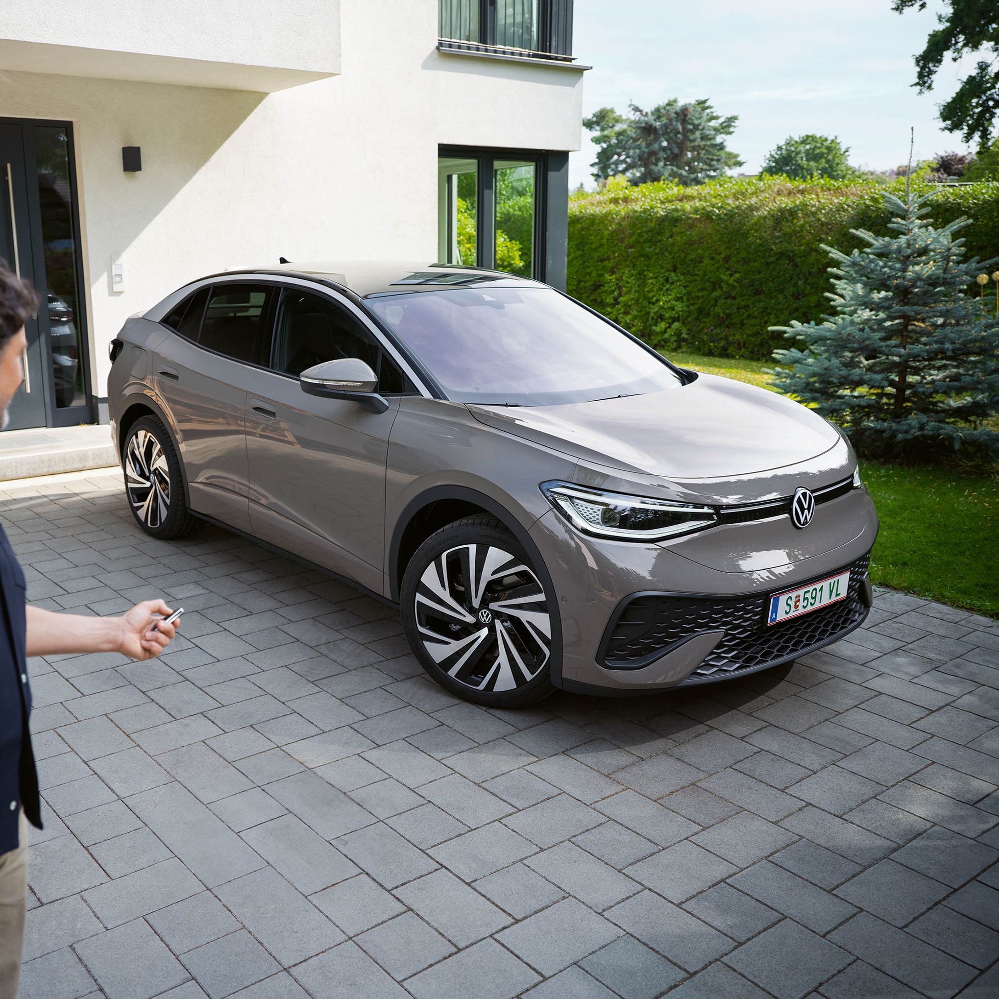 Ein grauer ID.5 steht in einer Einfahrt vor einem Haus, ein Mann schließt das Auto ab. 