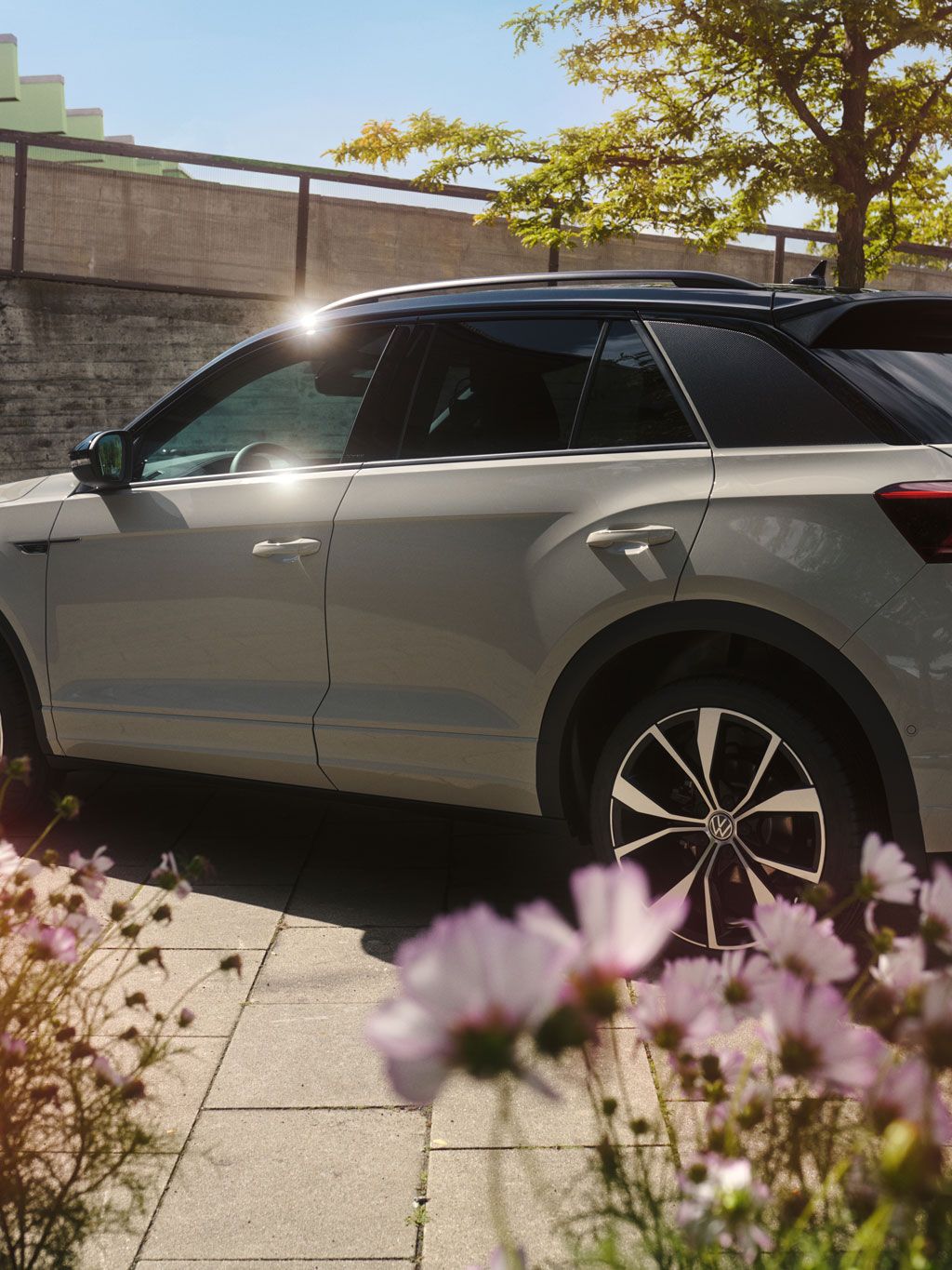 Blick auf die linke Seite und das Heck vom VW T-Roc, im Vordergrund blühen rosa Blumen 