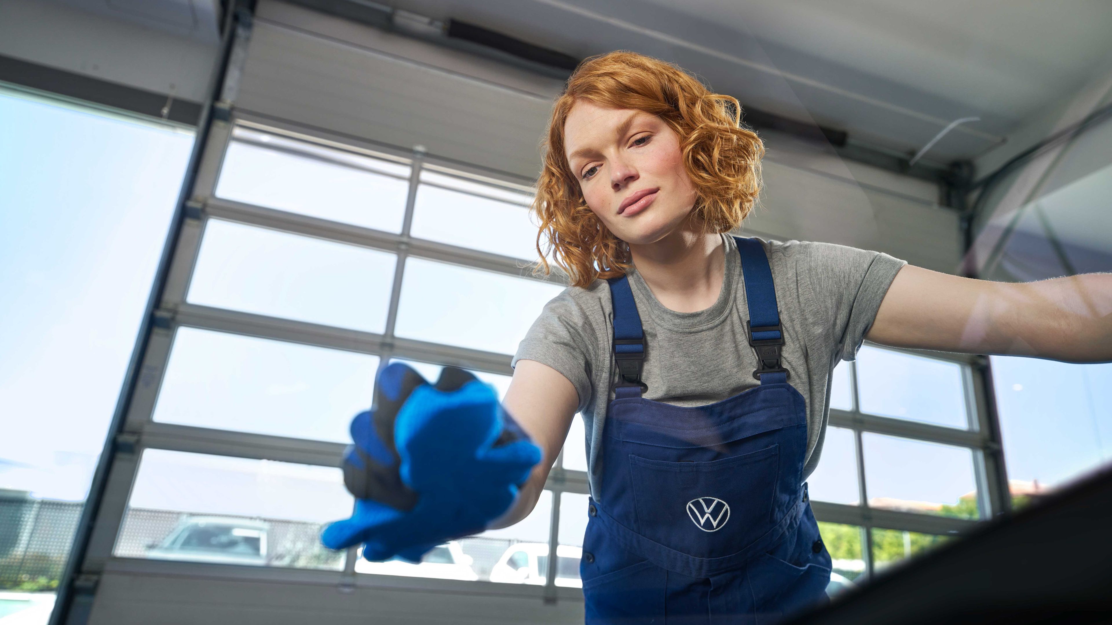 Eine Volkswagen Servicetechnikerin poliert die Frontscheibe eines Volkswagen