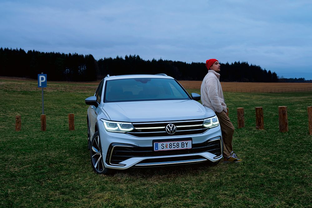 Ein weißer Tiguan Allspace ist geparkt auf einer Wiese, ein Mann lehnt sich an die Front des Autos an