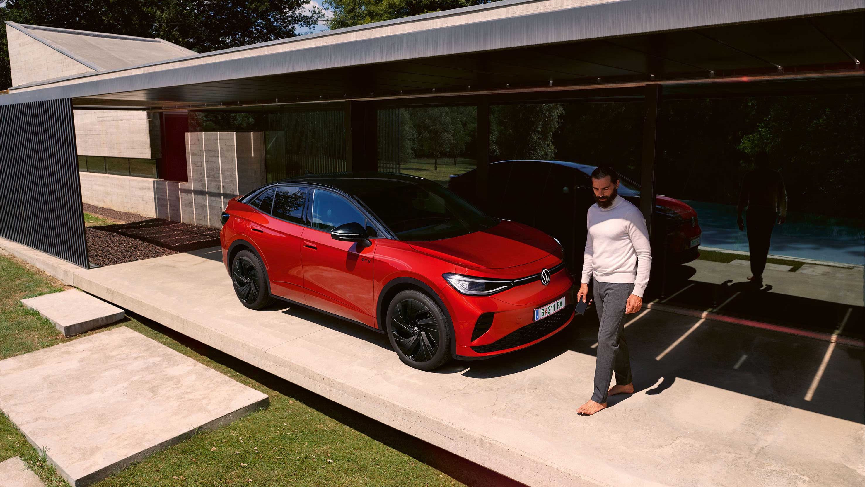 Roter VW ID.5 GTX von schräg vorne in einem modernen Carport, ein Mann geht vor der Motorhaube entlang