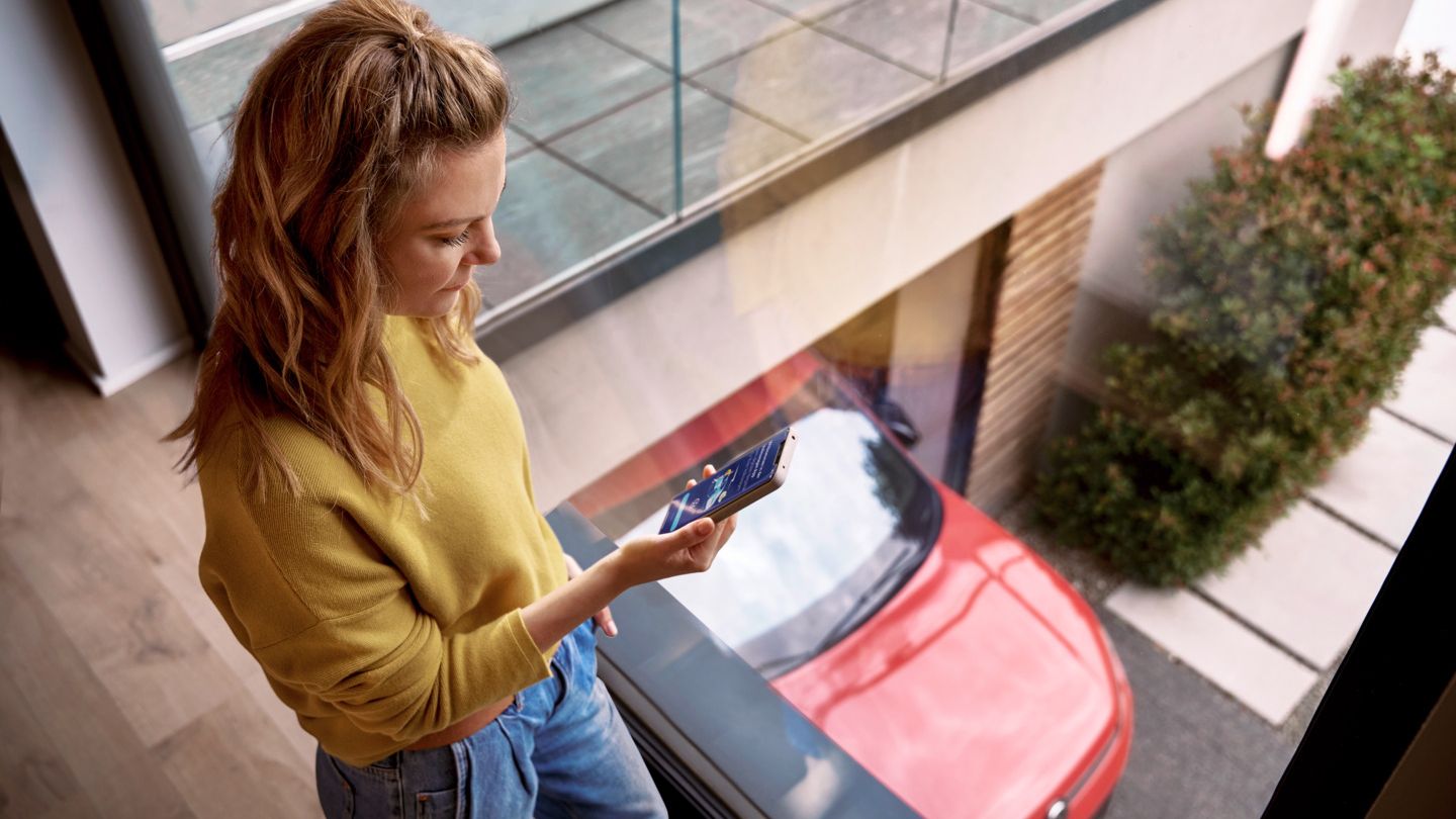 Frau schaut zu Hause auf ihr Smartphone, während ihr Tiguan in der Einfahrt geparkt ist