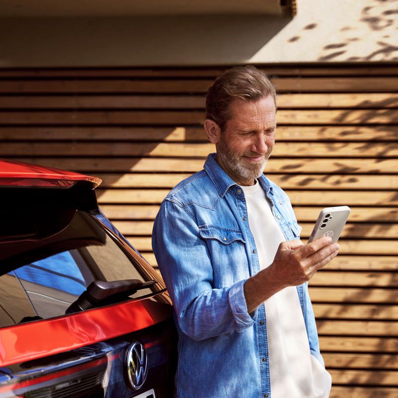 Mann schaut auf Handy vor seinem Volkswagen