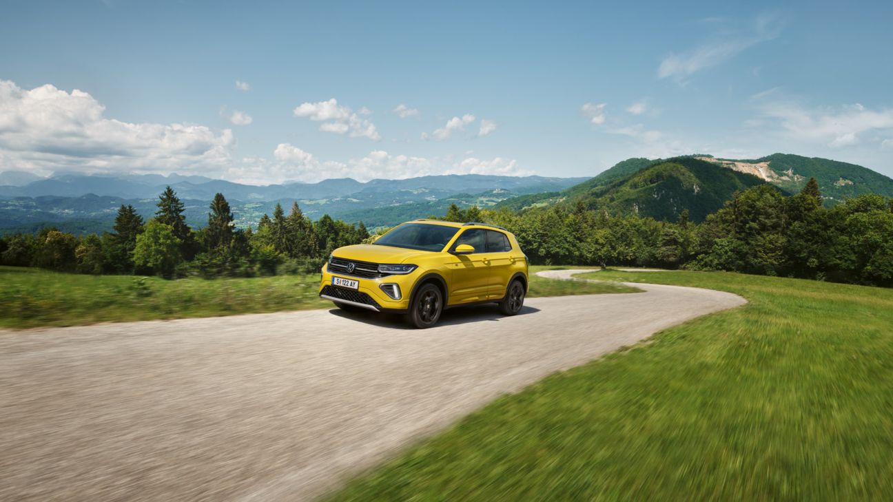 Ein gelber VW T-Cross auf einer Straße in hügeliger Landschaft.