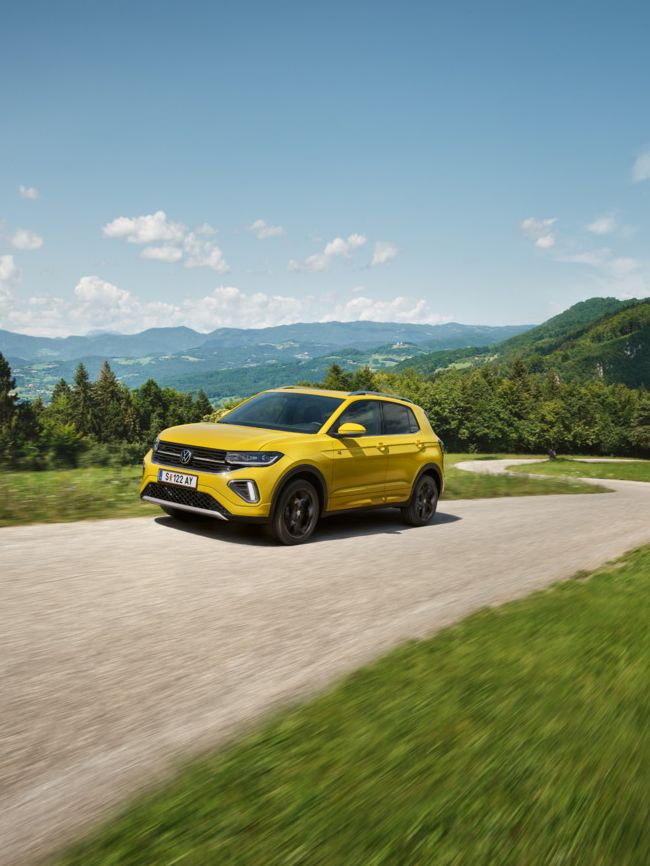 Ein gelber VW T-Cross auf einer Straße in hügeliger Landschaft.