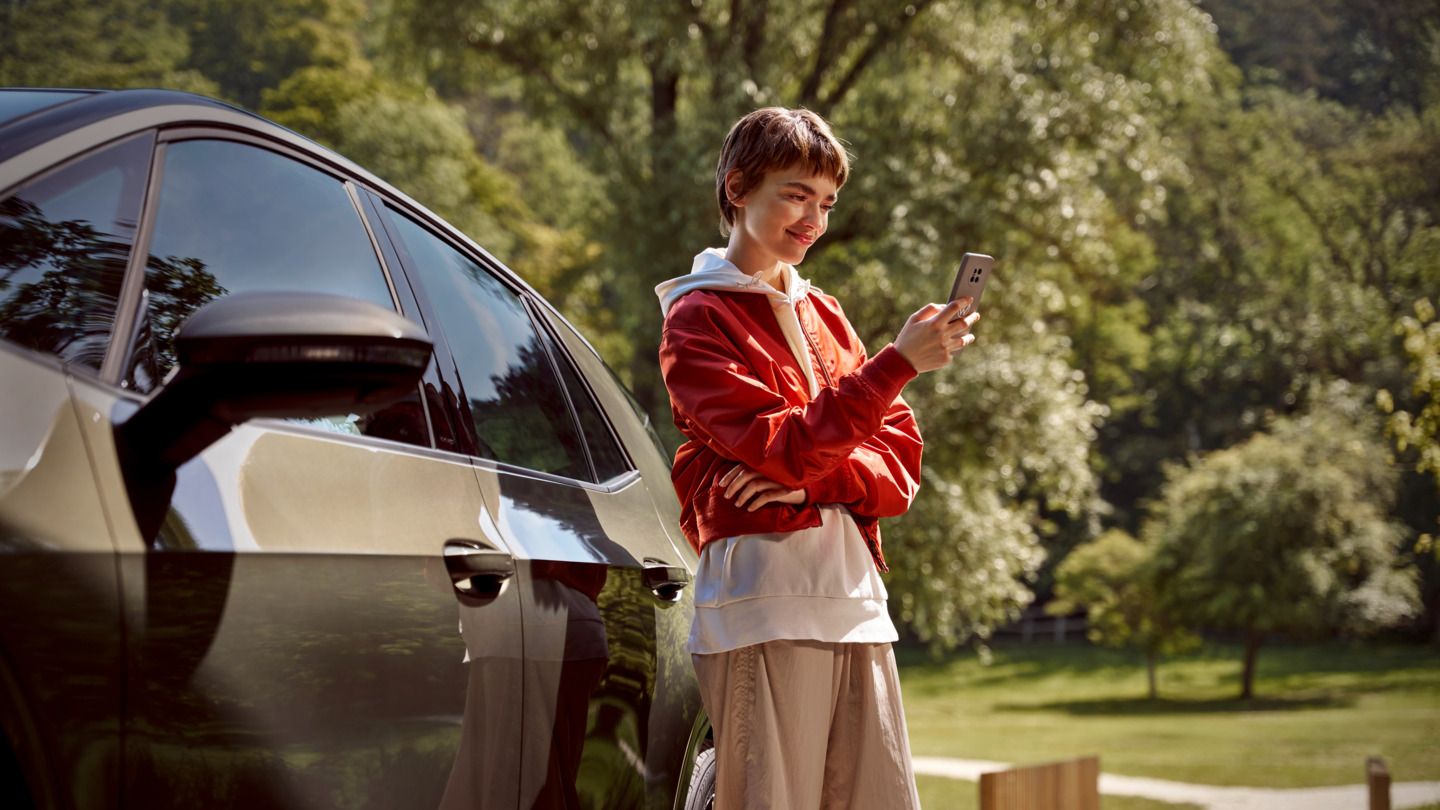 Eine Frau mit einem Smartphone steht neben ihrem ID.3