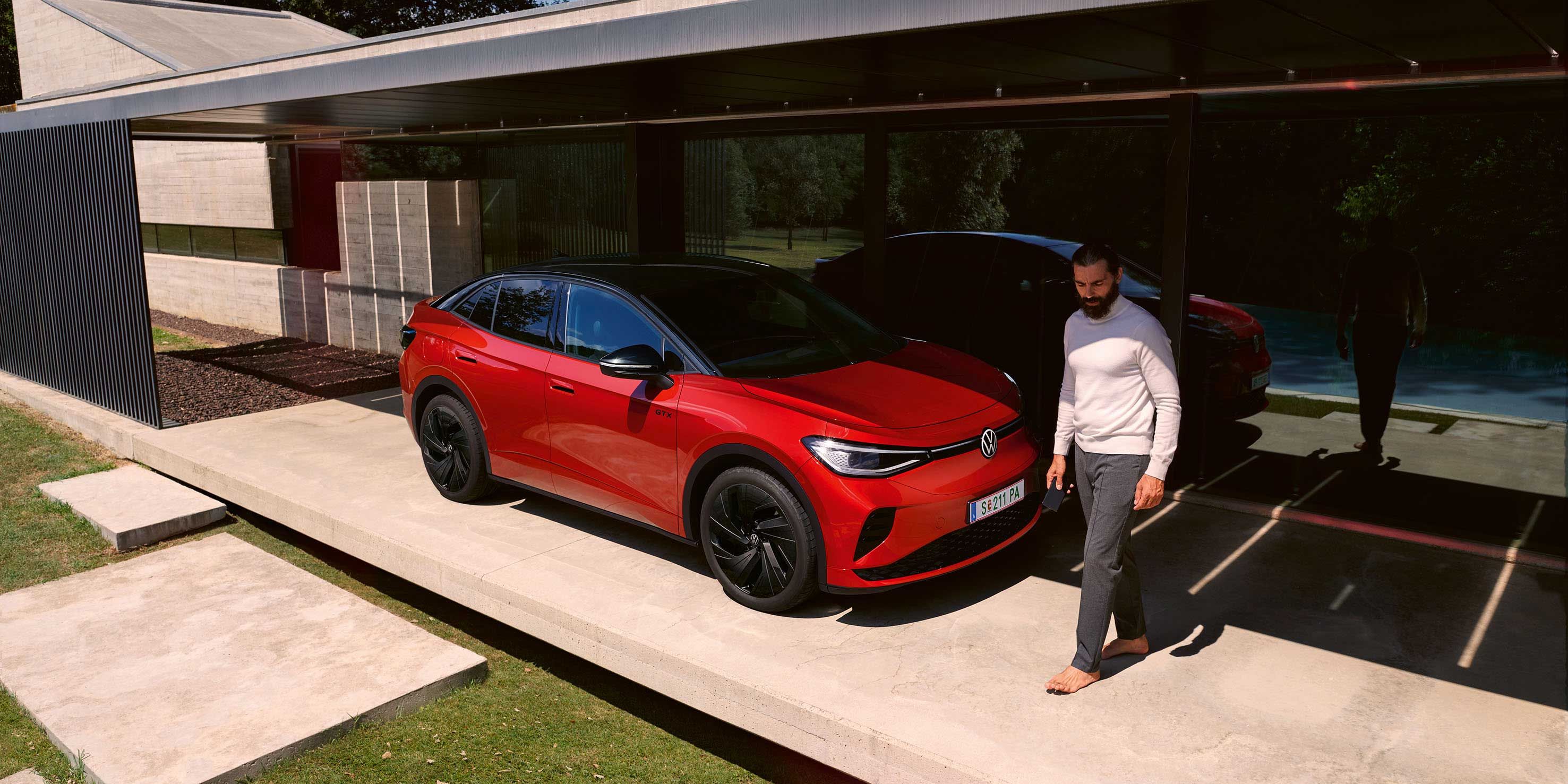 Roter VW ID.5 GTX von schräg vorne in einem modernen Carport, ein Mann geht vor der Motorhaube entlang