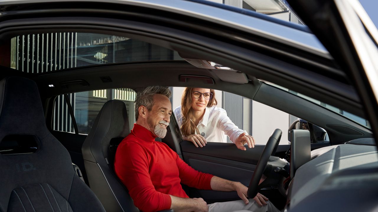 Ein Mann sitzt am Steuer eines Volkswagen und lächelt