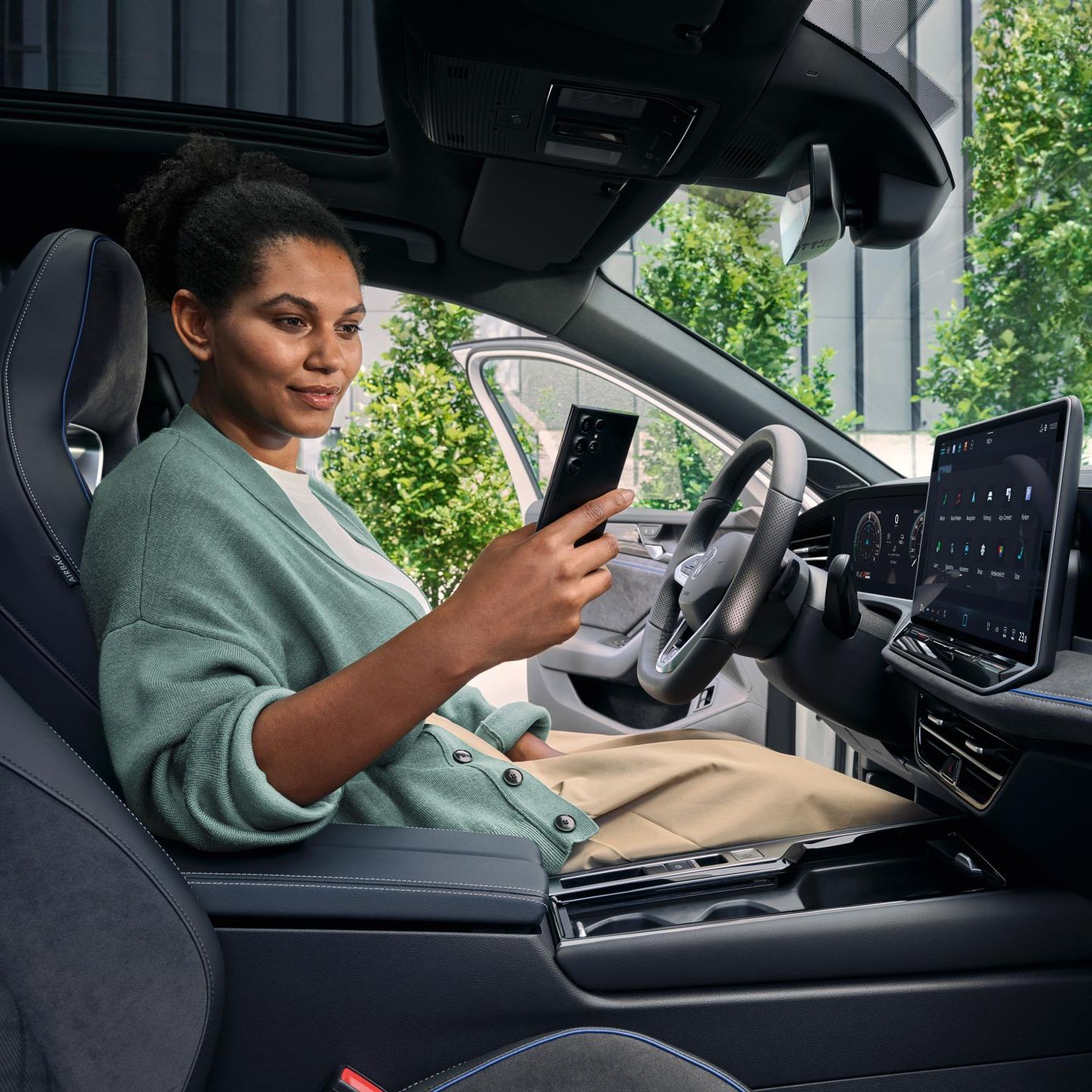 Eine Frau sitzt bei geöffneter Tür auf dem Fahrersitz des geparkten VW Passat und blickt auf ihr Smartphone.