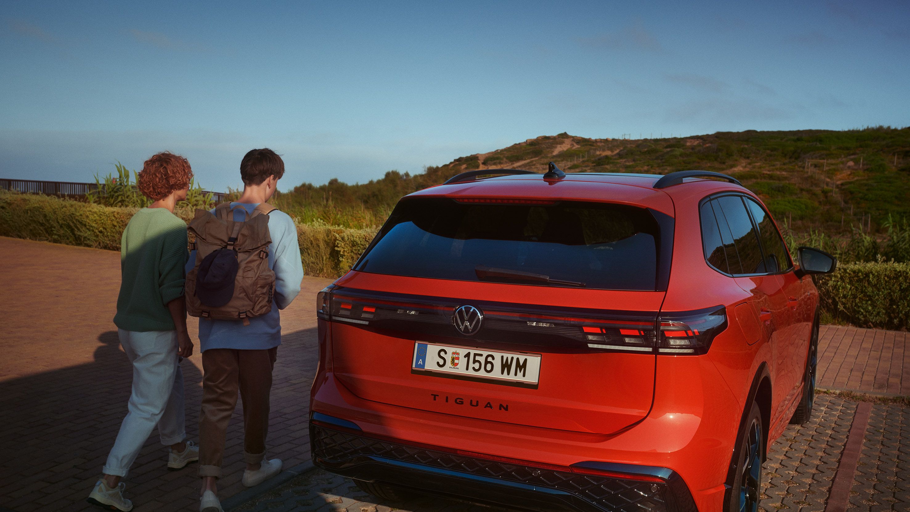 Heckansicht eines geparkten VW Tiguan. Eine Frau und ein Teenager gehen auf den Wagen zu. 