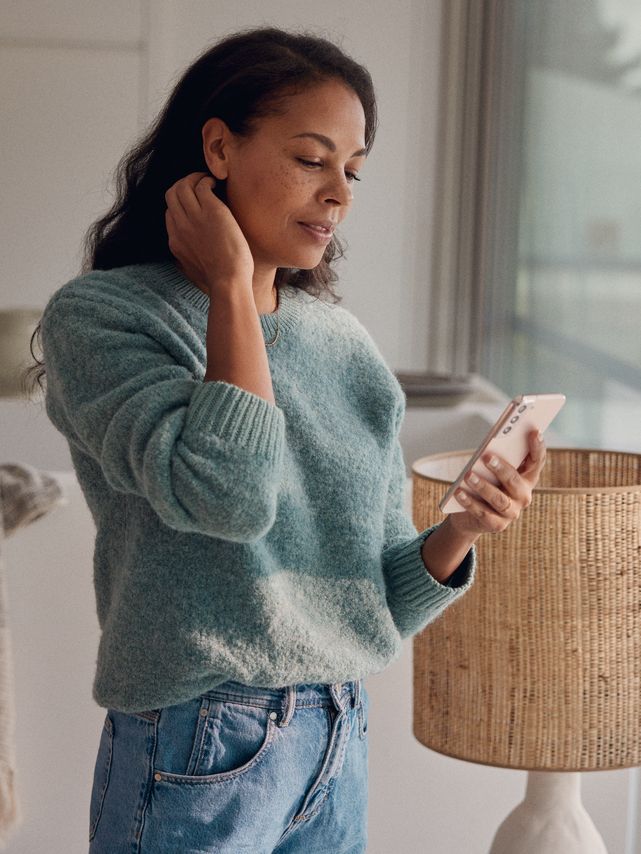 Eine Frau steht am Fenster und blickt auf ihr Smartphone