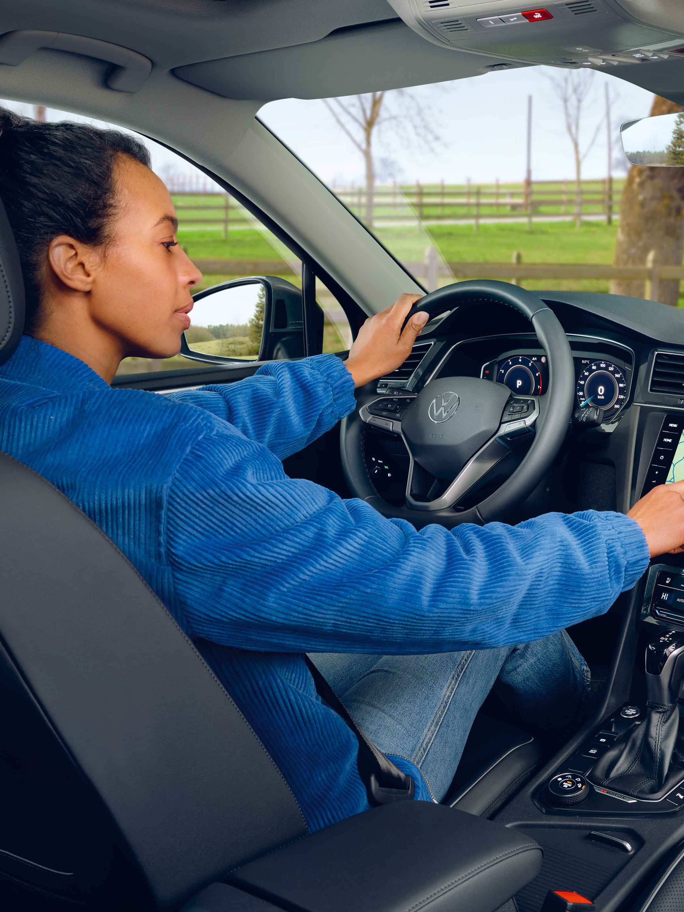 Eine Frau sitzt auf dem Fahrersitz des VW Tiguan Allspace und bedienet das Navigationssystem