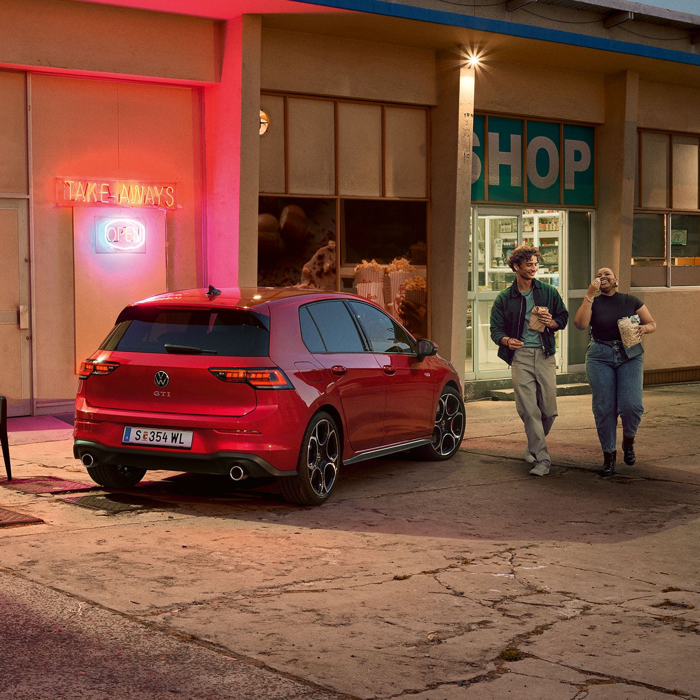 Heckansicht eines roten VW Golf GTI in abendlicher Stimmung, zwei Personen gehen neben ihm her