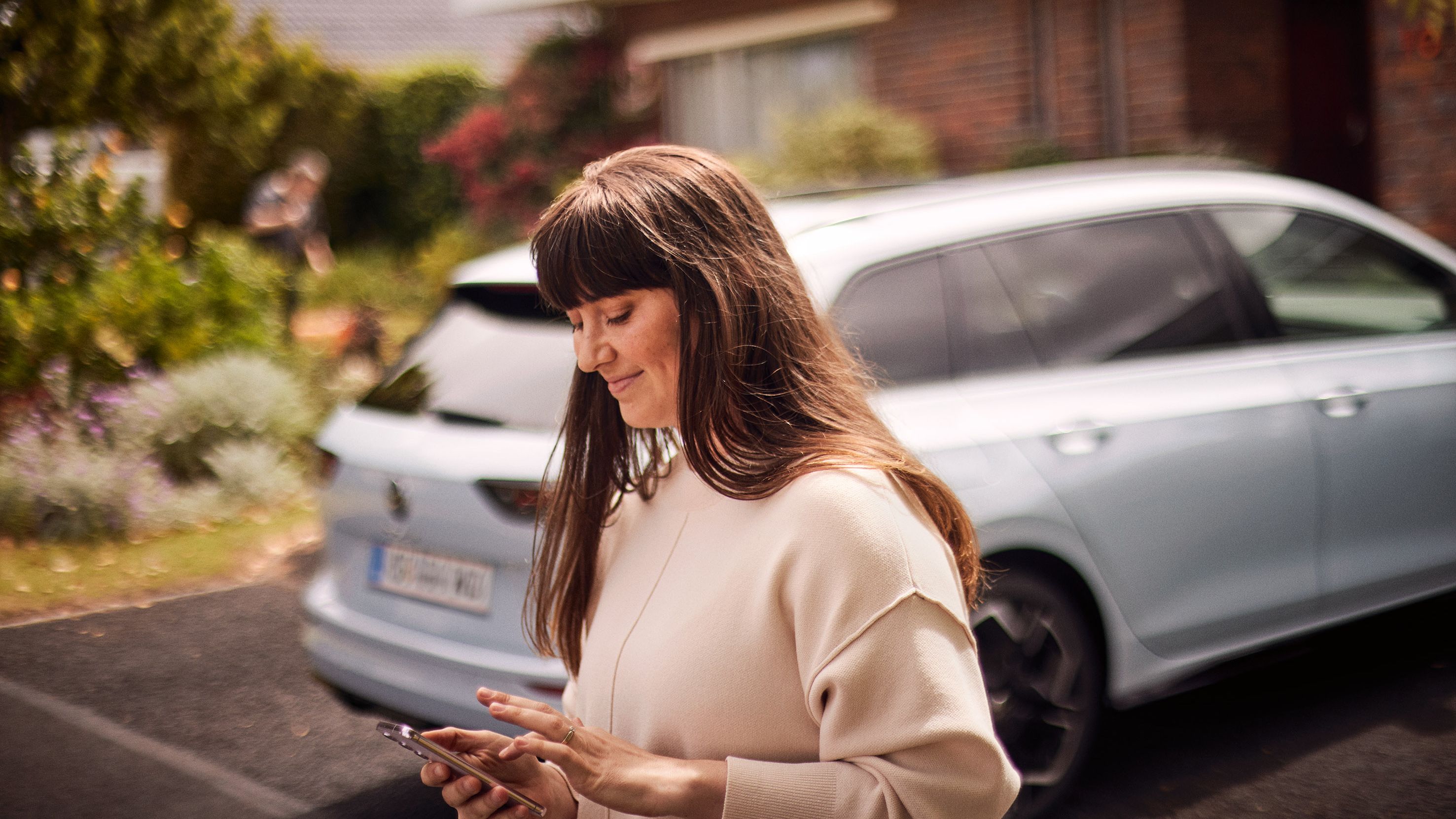 Frau steht vor VW Golf Variant und nutzt die Volkswagen App auf ihrem Smartphone