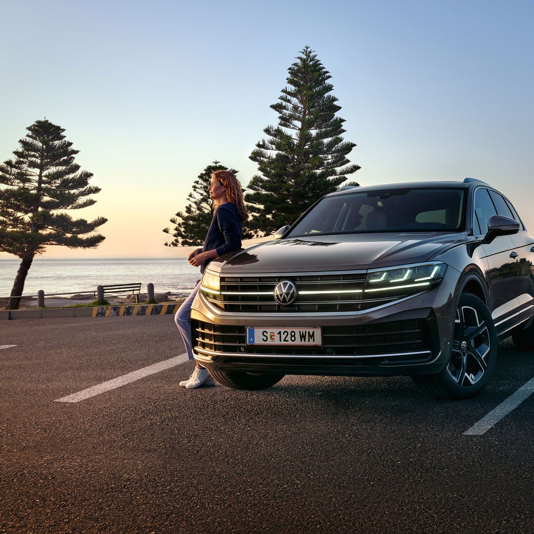 Ein VW Touareg Elegance in der Dämmerung am Meer mit eingeschalteten HD-Matrix-Scheinwerfern. 