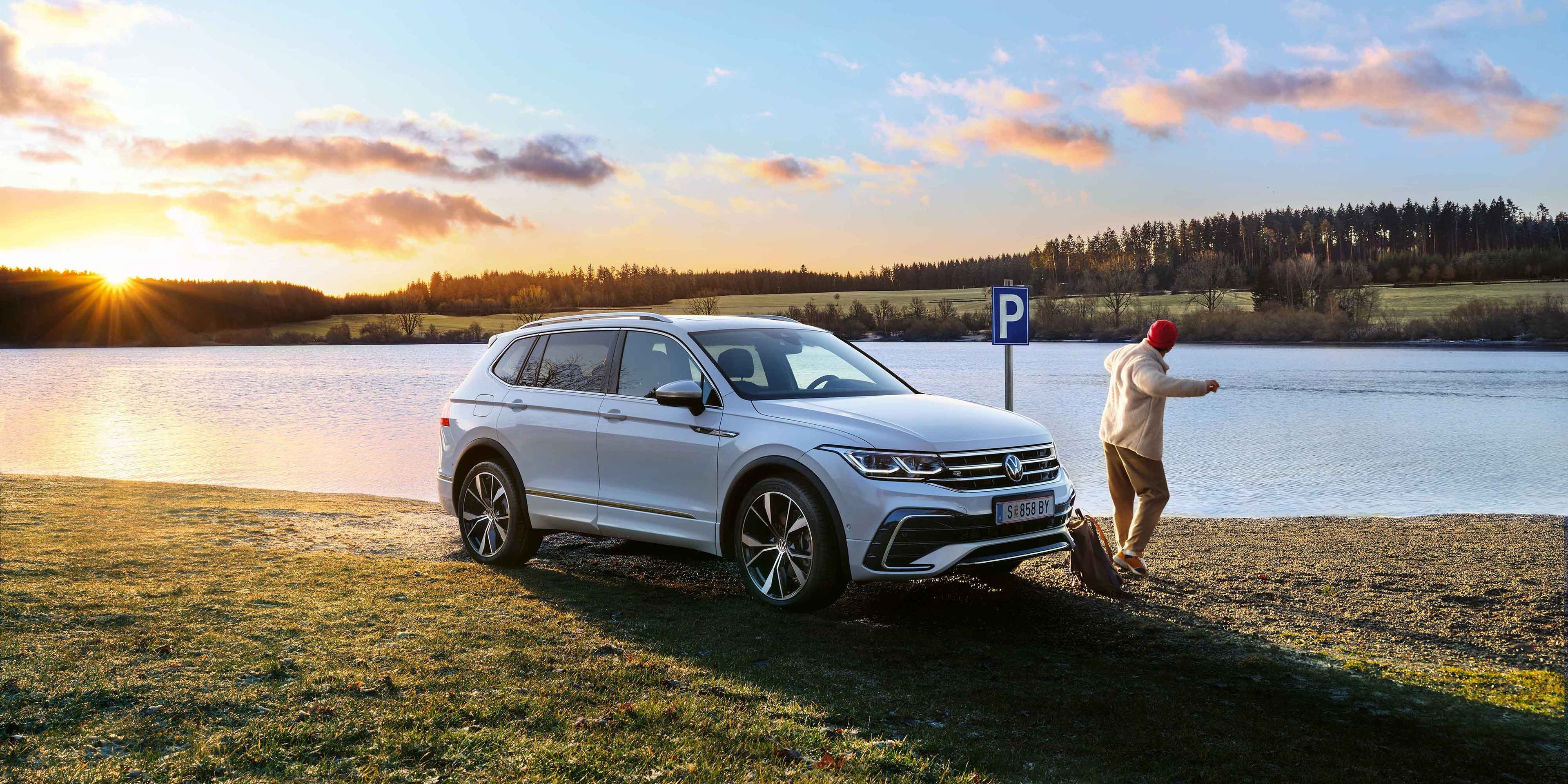 Mann steht neben einem weißen VW Tiguan Allspace, der am Seeufer geparkt ist