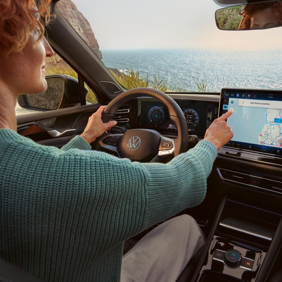  Eine Frau sitzt im VW Tiguan und bedienet das Infotainmentsystem mit Navigationsfunktion.