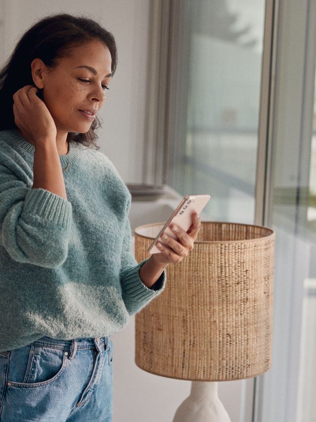 Eine Frau steht am Fenster und blickt auf ihr Smartphone