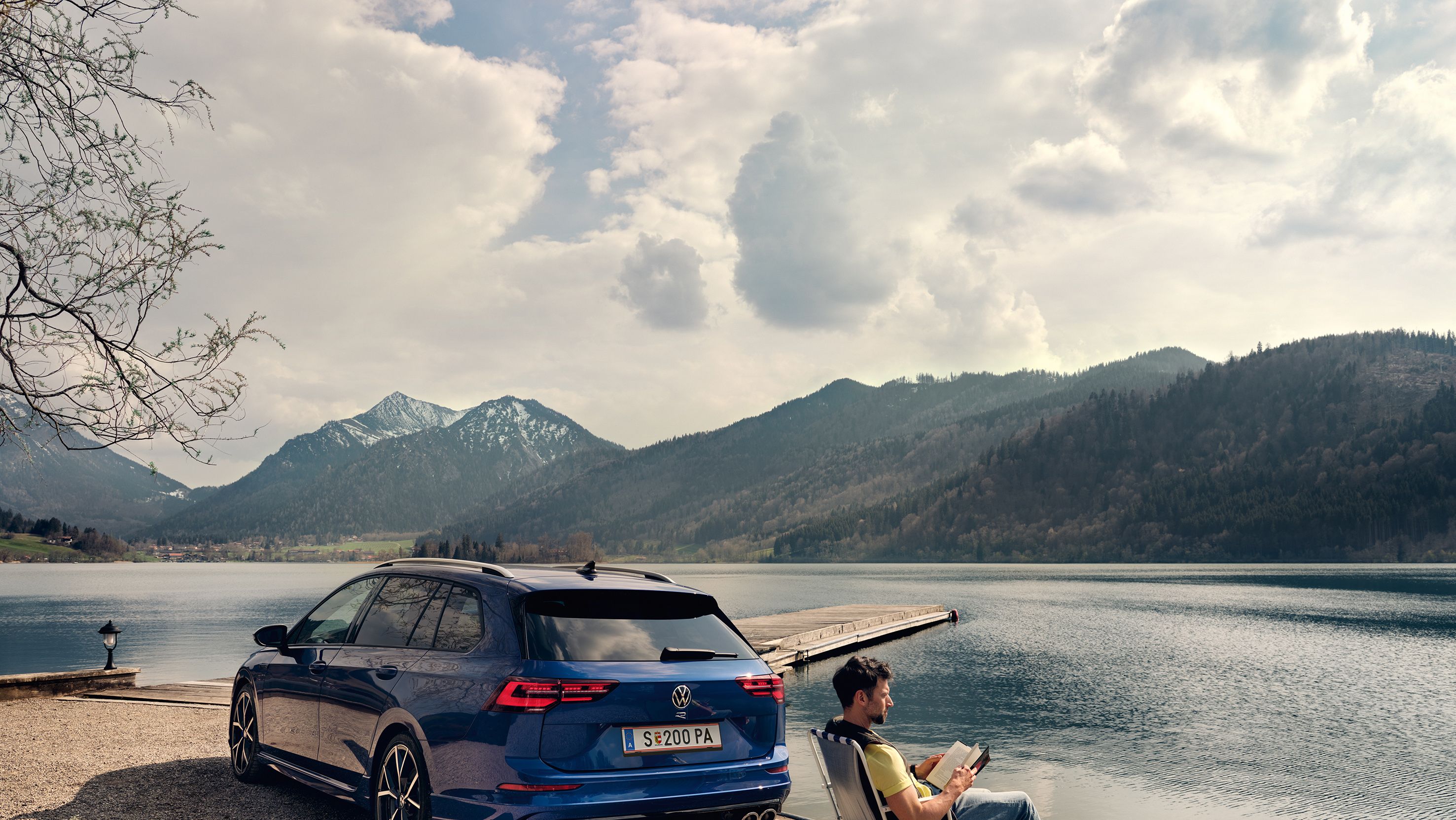 VW Golf R Variant steht an einem See, daneben sitzt ein Mann in einem Campingstuhl