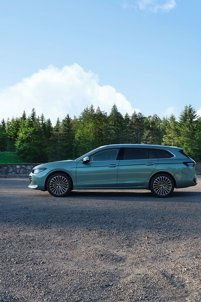 Ein grüner VW Passat B9 in der Seitenansicht, im Hintergrund zwei Menschen und Wald