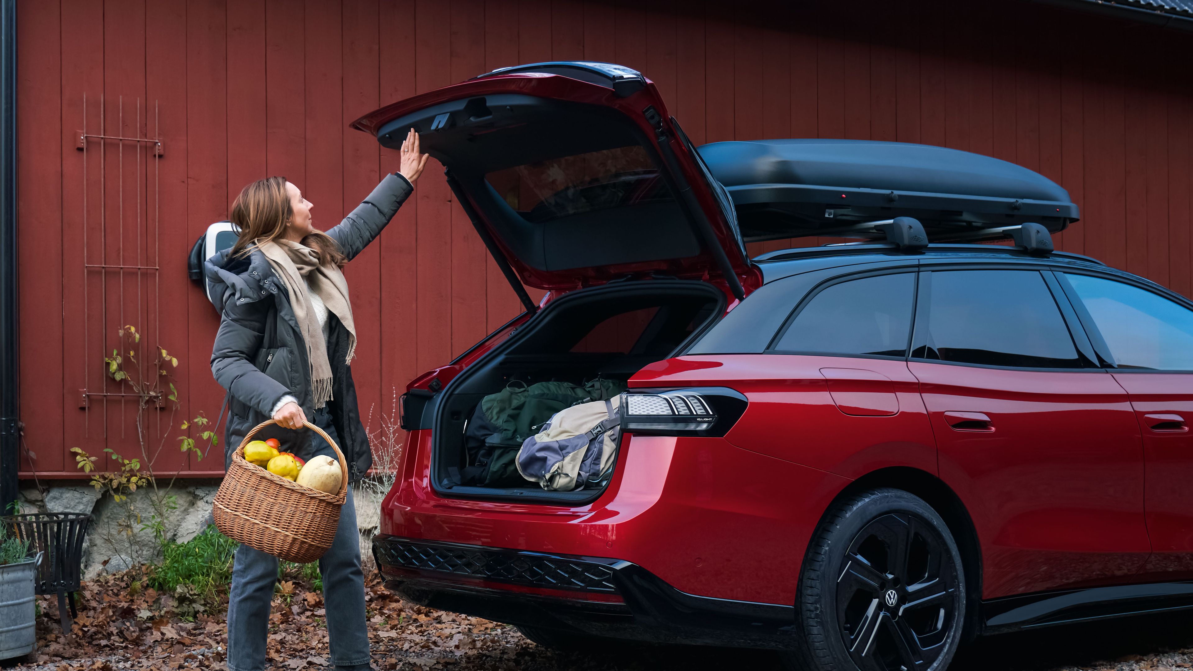 Ein roter Volkswagen Passat mit Dachbox, eine Frau mit Obstkorb in der Hand schließt den Kofferraum