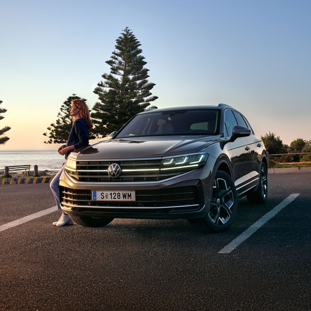 Ein VW Touareg Elegance in der Dämmerung am Meer mit eingeschalteten HD-Matrix-Scheinwerfern. 