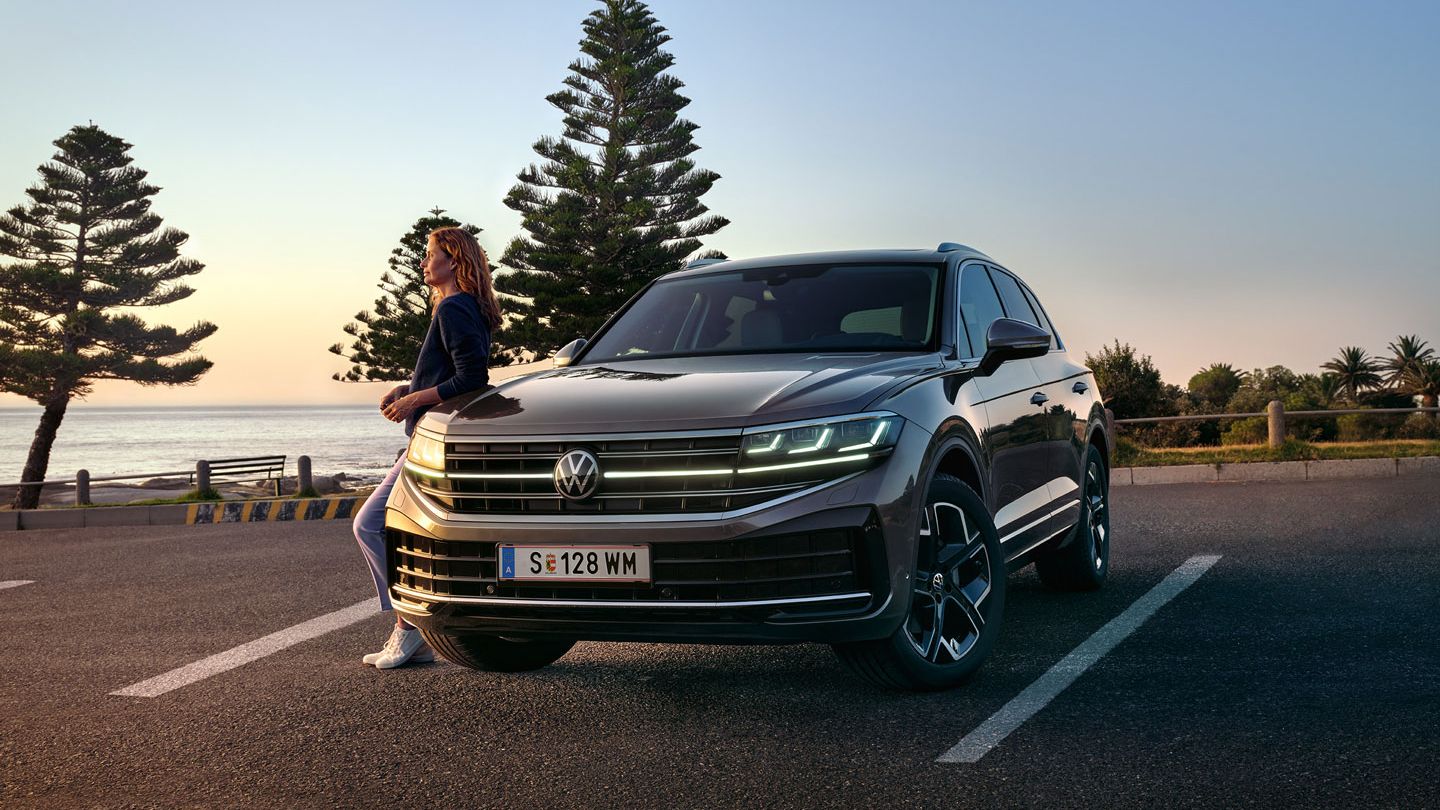 Ein VW Touareg Elegance in der Dämmerung am Meer mit eingeschalteten HD-Matrix-Scheinwerfern. 