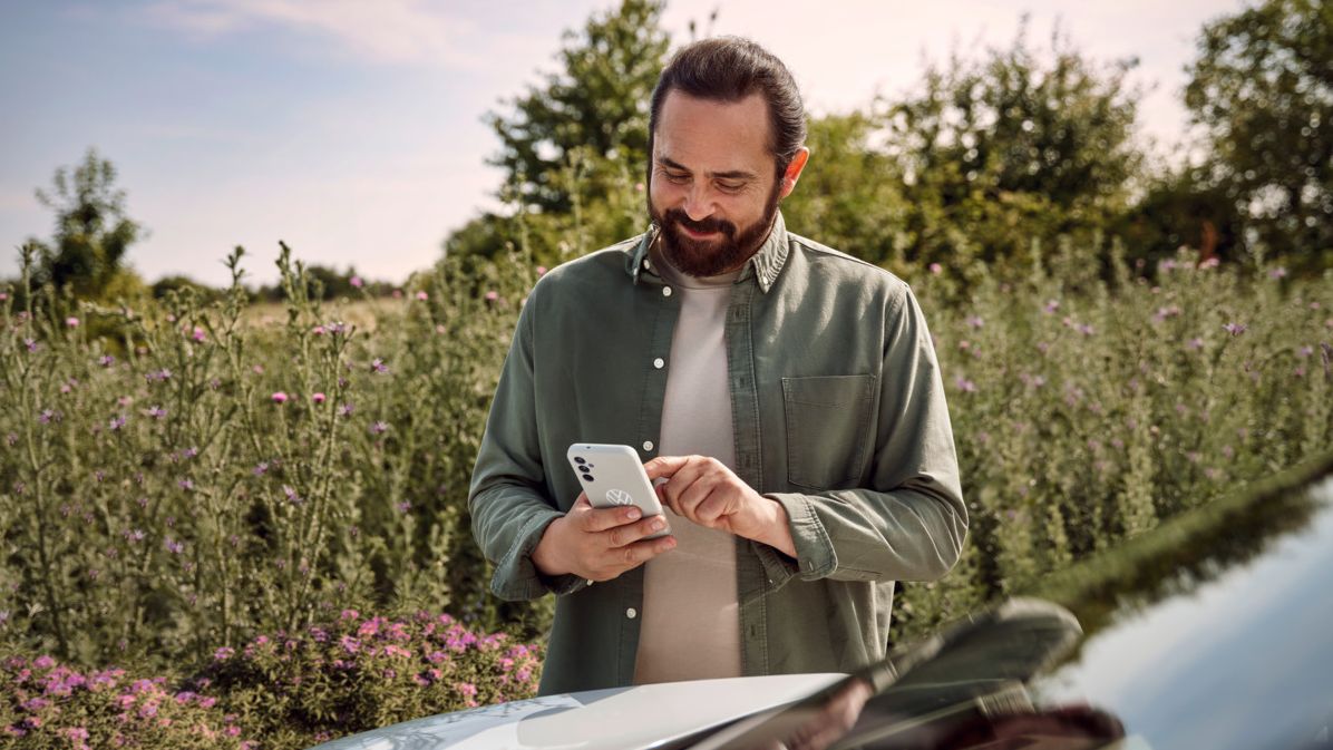  Ein Mann mit einem Smartphone in der Hand steht neben seinem ID.4